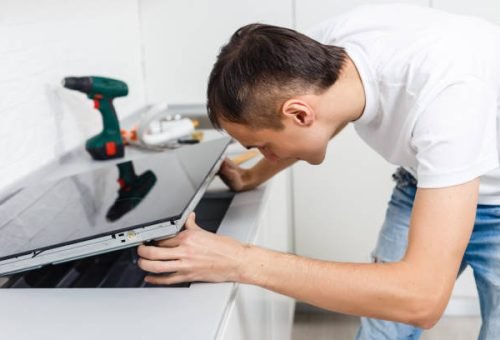 Young repairman installing induction cooker in kitchen
