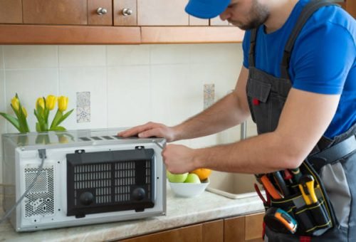 Young repairman fixing and repairing microwave oven by screwdriver in kitchen.