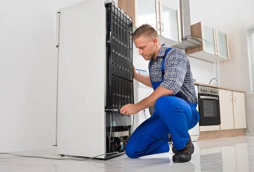 Male Worker Repairing Refrigerator With Screwdriver In House
